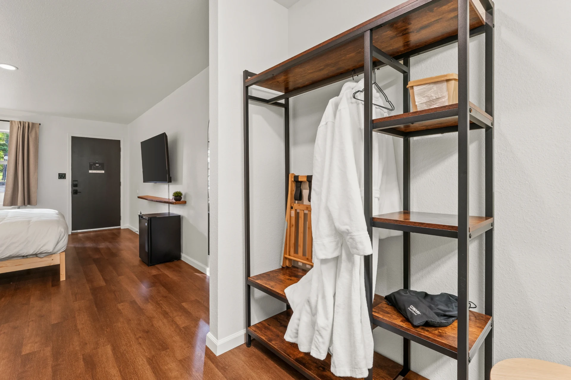 Open wardrobe with plush white robes and a mini fridge in the background