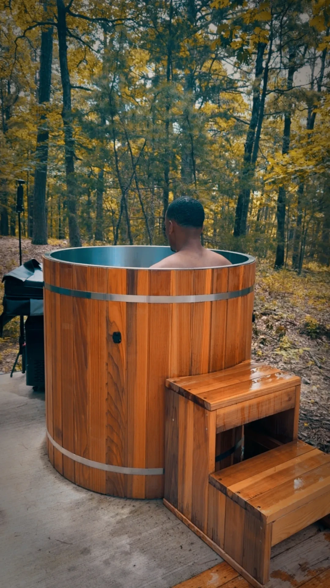 Guest sitting in the cedar cold plunge surrounded by autumn trees
