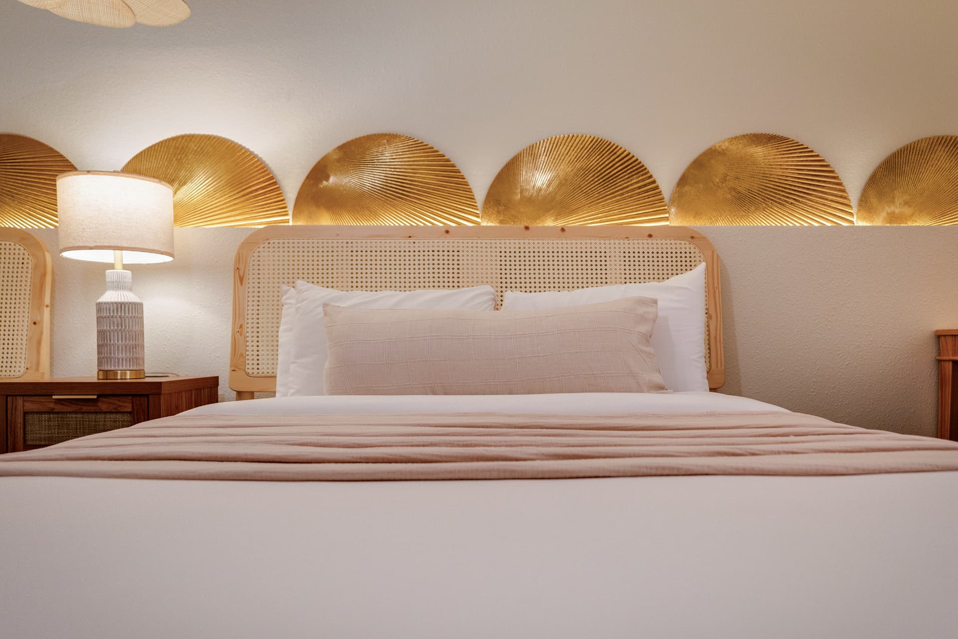 Queen bed with cane headboard and brass fan wall art