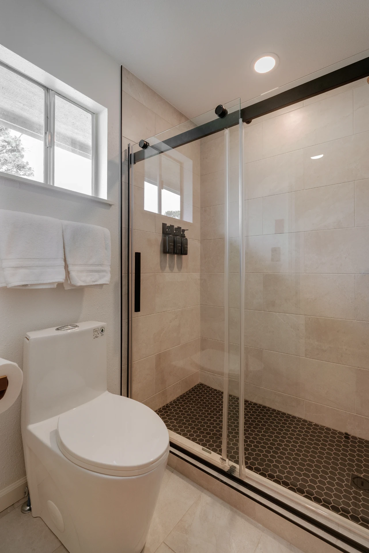 Walk-in glass shower with black hexagon tile floor