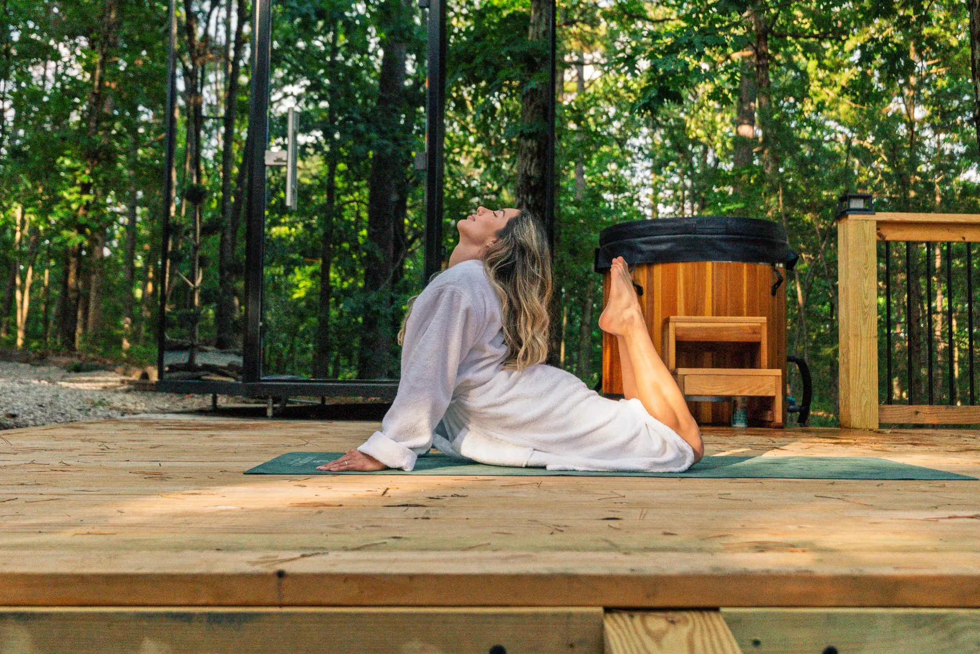 Guest in a robe practicing yoga on the wooden deck beside the cold plunge