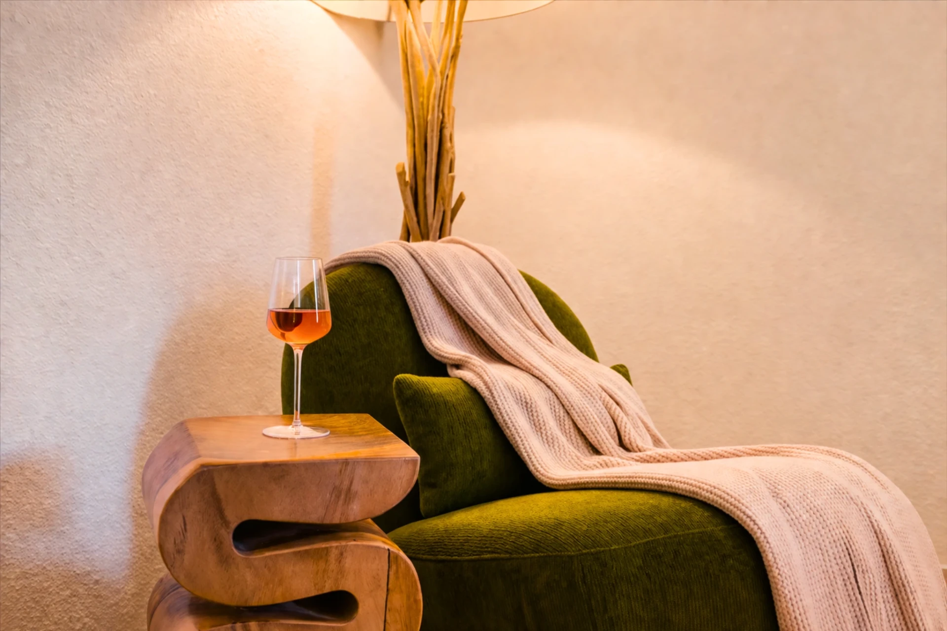 Green velvet armchair with a throw blanket and a glass of wine