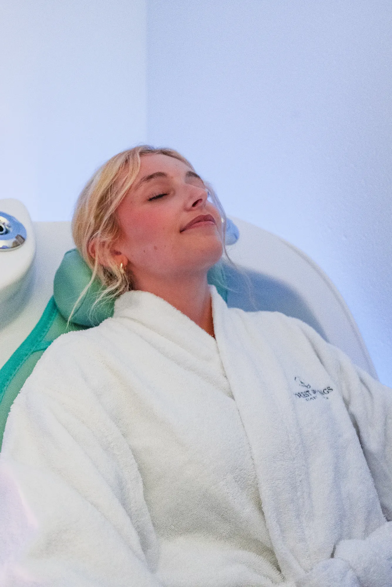 Guest in a white Forest Springs robe resting with eyes closed in the infrared therapy pod