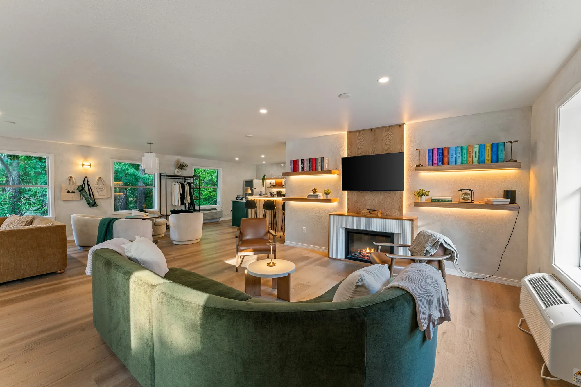 Forest Lounge interior at Forest Springs Resort with a curved green sofa, armchairs and a lit fireplace below shelves of books