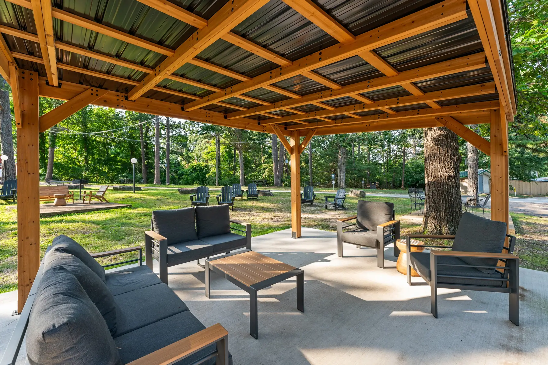 Covered outdoor lounge at Forest Springs Resort with timber posts, outdoor sofas and coffee tables, opening onto the lawn and pines