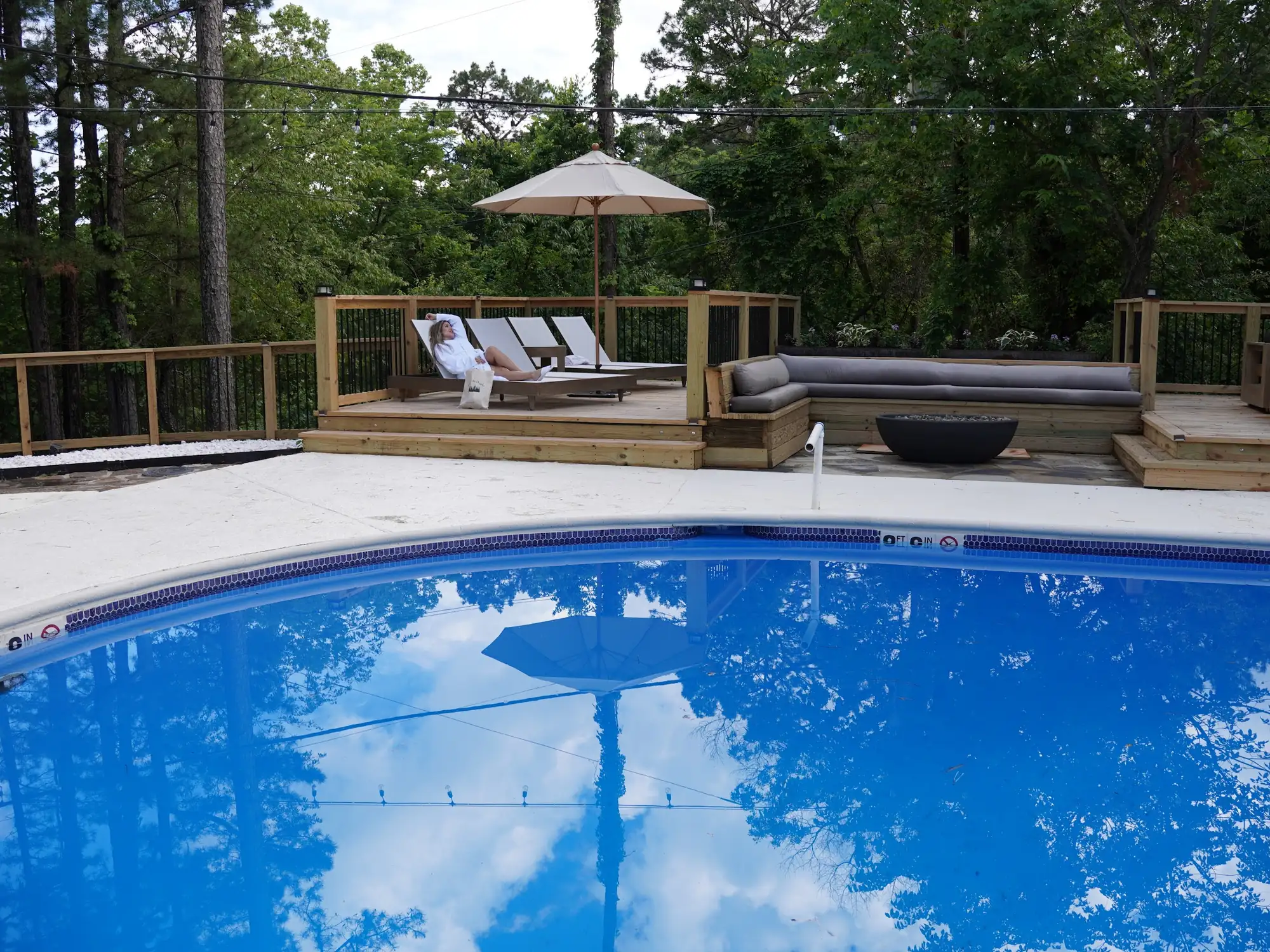 Outdoor pool at Forest Springs Resort with a raised wooden deck, umbrella, sun loungers and lounge seating among the trees