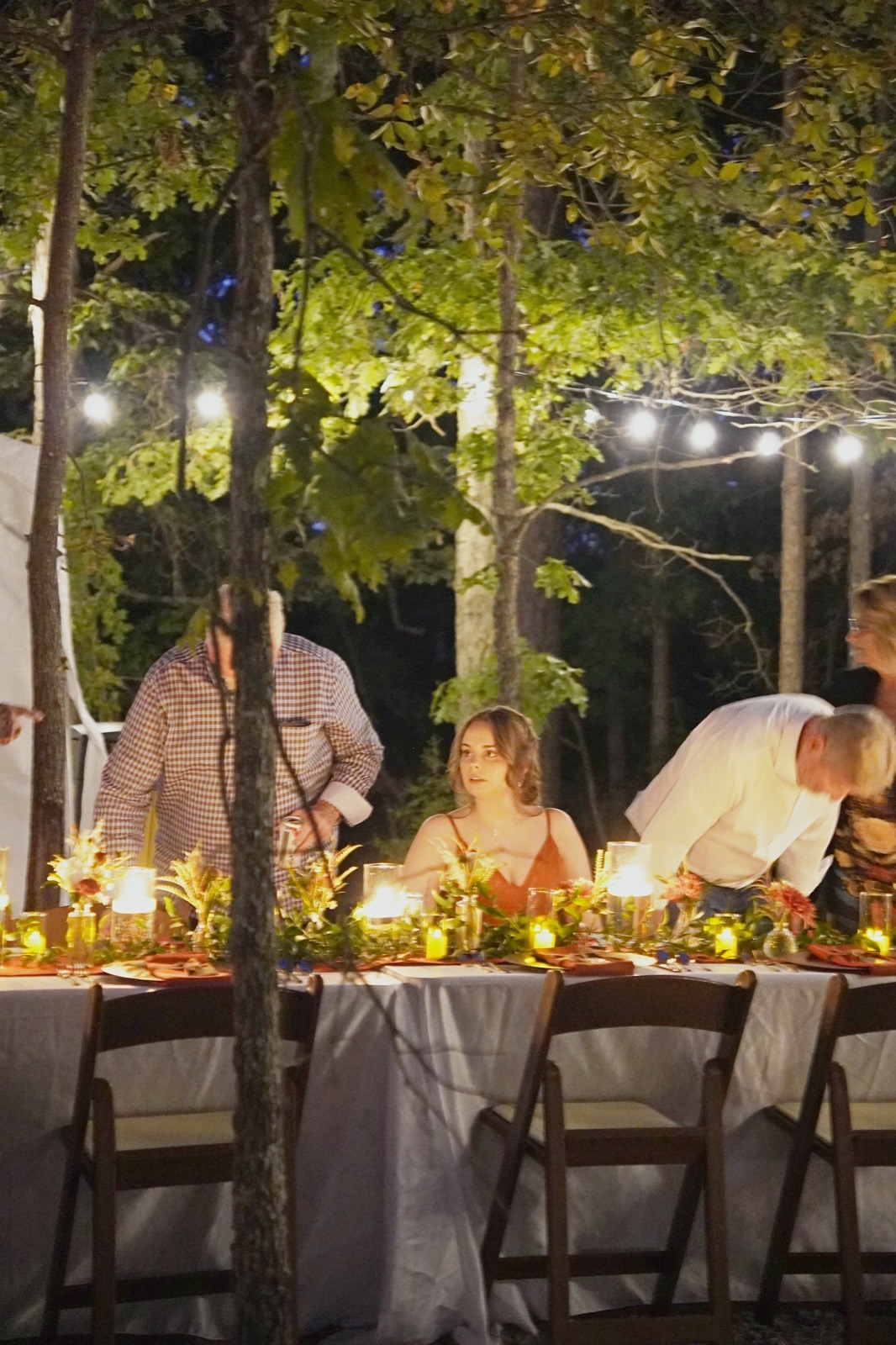 Guests at a long dinner table beneath string lights in the forest at Forest Springs Resort